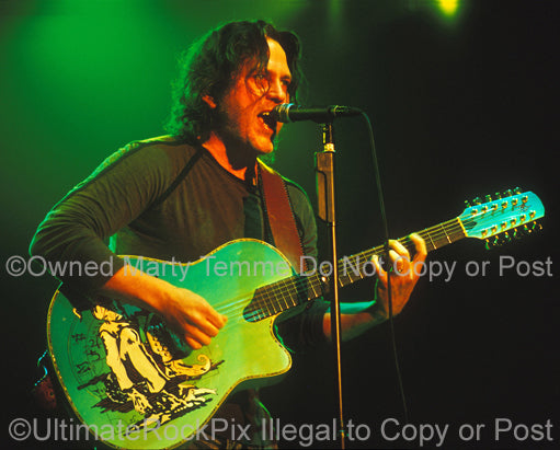 Photo of Kip Winger playing an acoustic 12 string guitar in concert by Marty Temme