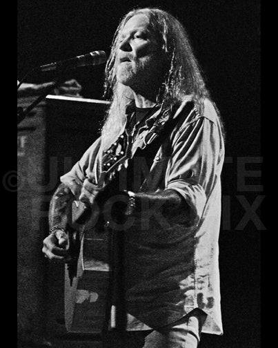 Photo of Gregg Allman playing acoustic guitar in concert by Marty Temme